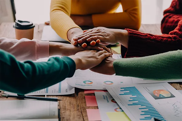 A close-up of a diverse team stacking hands over charts and data, symbolizing Alcateia’s core values of partnership, transparency, and shared success with construction clients.
