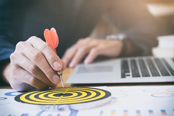 A hand aiming a dart at a bullseye target, representing Alcateia’s mission of delivering precise marketing results and predictable leads for contractors in Massachusetts.